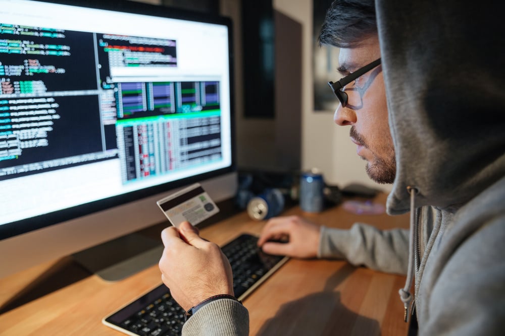 Concentrated young hacker in glasses stealing money from different credit cards sitting in dark room Concentrated young hacker in glasses stealing money from different credit cards sitting in dark room