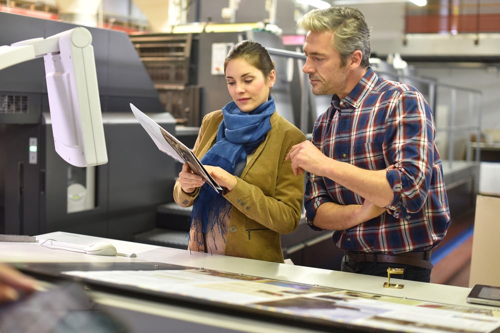 Man in printing house showing client printed documents Man in printing house showing client printed documents